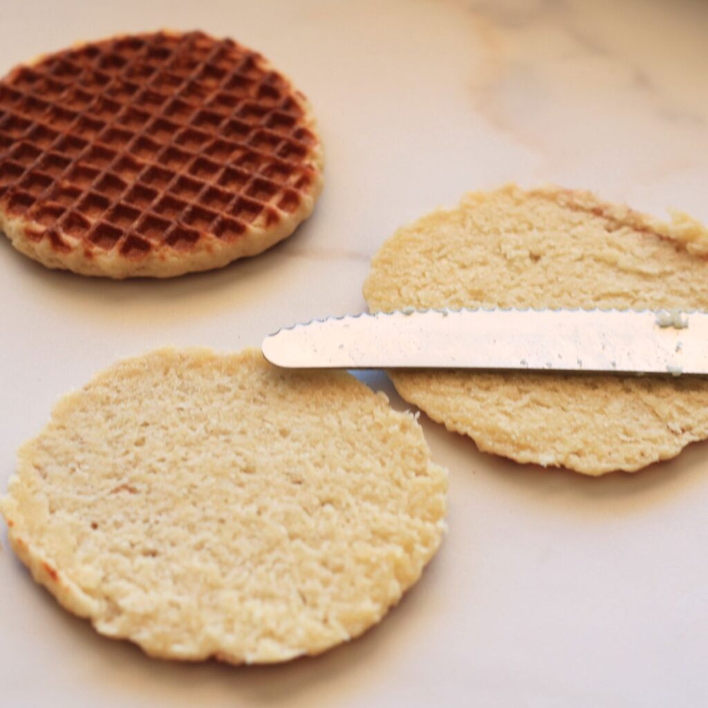 Two waffle cookies on the counter one cut open with a serrated knife laying on top of it.