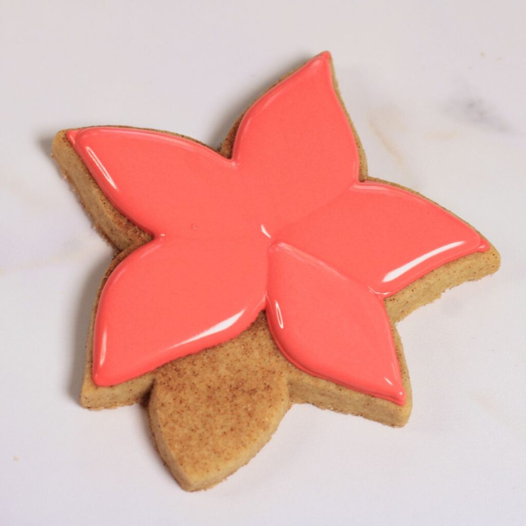 Poinsettia flower shaped cookie with five petals filled in with red icing.