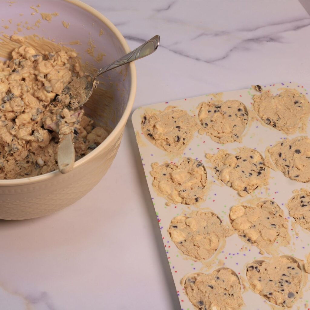 A large mixing bowl filled with avalanche bark ingredients, spoon, and spatula sitting next to a tray with heart shaped cavities filled with same mixture from bowl.