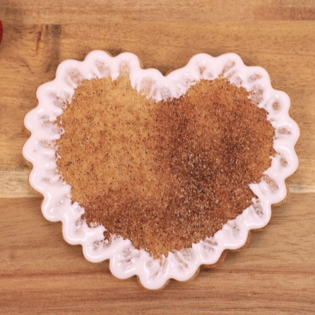 A scalloped heart shaped cookie with white icing outlining the scallops. The icing is spread  towards the center of the cookie.